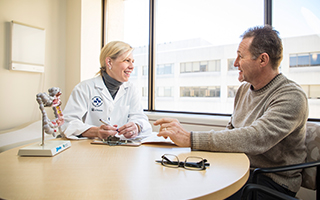 New head of cancer research, Dr. Rebecca Auer, sits at a table with a patient.